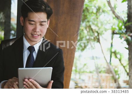 businessman in suit holding touchpad while standing outside building. young asian man using digital tablet for work outdoors businessman in suit holding touchpad while standing outside building. young asian man using digital tablet for work outdoors 38313485