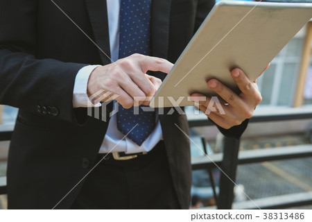 businessman in suit holding touchpad while standing outside building. young asian man using digital tablet for work outdoors businessman in suit holding touchpad while standing outside building. young asian man using digital tablet for work outdoors 38313486