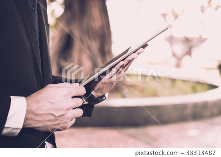 businessman in suit holding touchpad while standing outside building. young asian man using digital tablet for work outdoors businessman in suit holding touchpad while standing outside building. young asian man using digital tablet for work outdoors 38313487