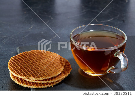 A glass cup of black tea with waffles on a dark 38320511