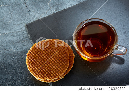 A glass cup of black tea with waffles on a dark 38320521