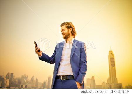 Western businessman using a phone on a rooftop with blurry city Western businessman using a phone on a rooftop with blurry city 38331909