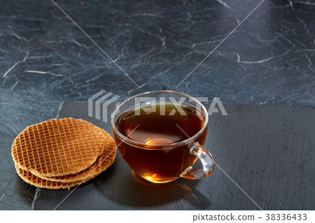A glass cup of black tea with waffles on a dark A glass cup of black tea with waffles on a dark 38336433