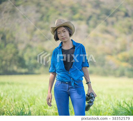 Woman wear hat and hold binocular in grass field 38352579