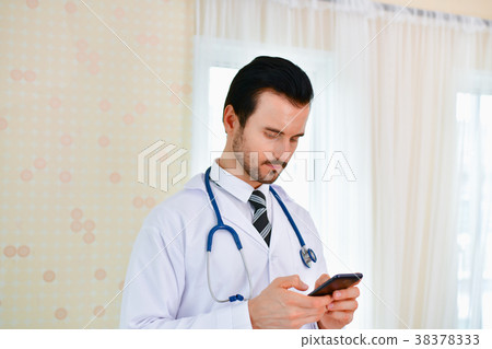 Smiling doctor posing in the office, he is wearing a stethoscope Smiling doctor posing in the office, he is wearing a stethoscope 38378333