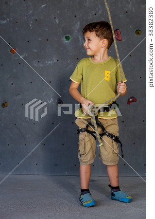 little boy standing near a climbing  rock wall indoor. 38382380