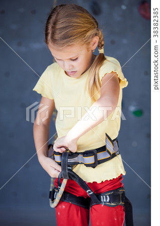 little girl standing near a climbing  rock wall indoor. 38382385