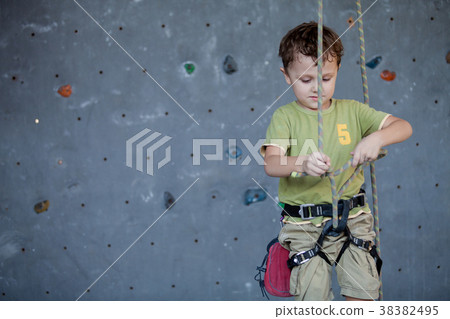 little boy standing near a climbing  rock wall indoor. 38382495