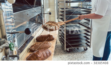 Woman in bakery putting bread on board Woman in bakery putting bread on board 38385408