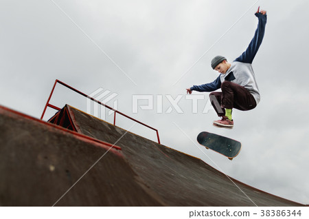 Teenager skateboarder in a cap doing a trick jump 38386344