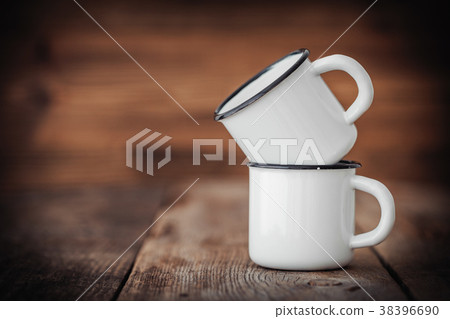 Two enameled cups on wooden rustic kitchen table. 38396690