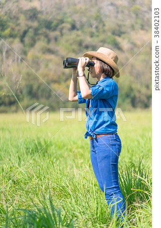 Woman wear hat and hold binocular in grass field Woman wear hat and hold binocular in grass field 38402103