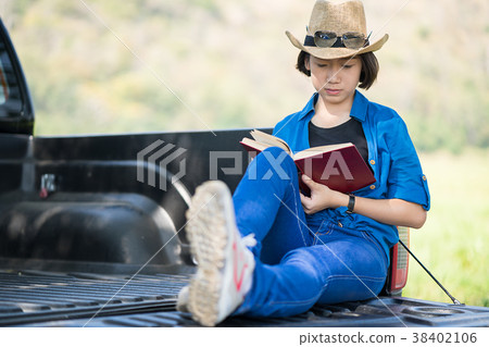 Woman wear hat and reading the book on pickup truck 38402106