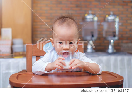 Toddler in high chair drinking milk in a glass 38408327