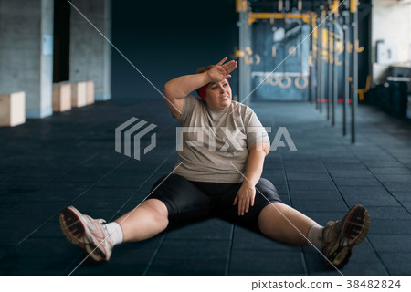 Tired overweight woman sits on the floor in gym 38482824