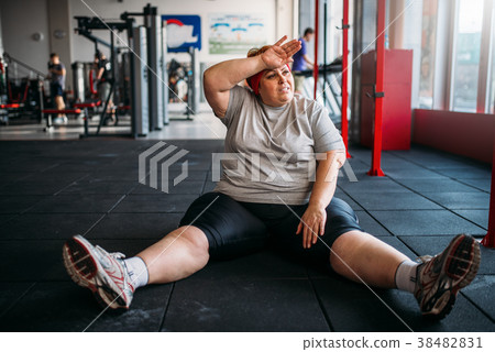 Tired overweight woman sits on the floor in gym 38482831