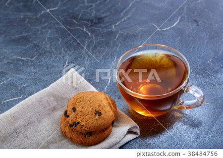 A glass cup of black tea with cookies on a dark 38484756