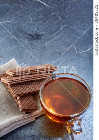 A glass cup of black tea with cookies on a dark 38485322