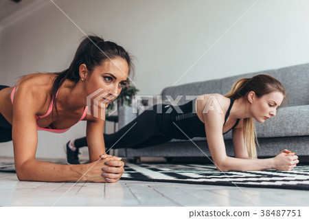Two fit women standing in plank position on floor Two fit women standing in plank position on floor 38487751