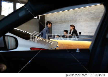 Staff and customers speaking at car dealership counter 38503591