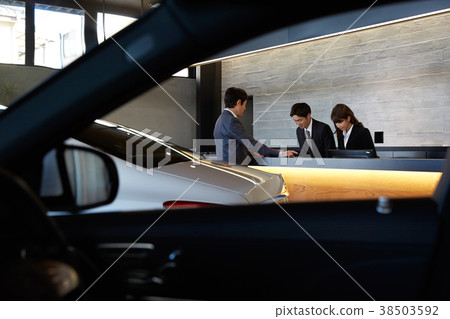Staff and customers speaking at car dealership counter 38503592