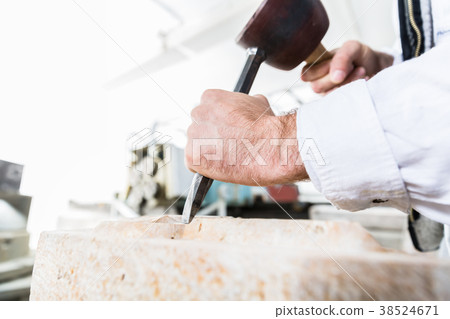 Stonemason cutting boulder with hammer and chisel 38524671