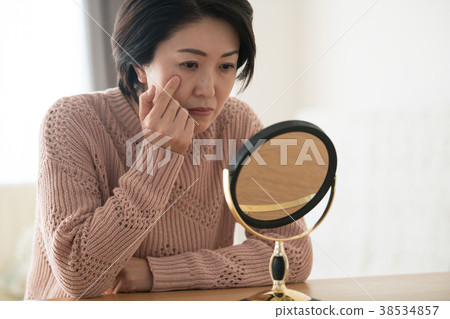 Middle woman looking at mirror with care for skin 38534857