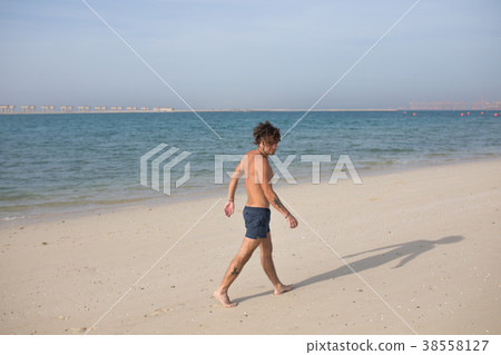 Young man walking along the beach. Young man walking along the beach. 38558127