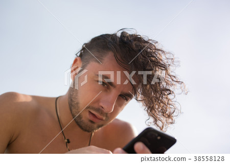 A man with curly hair uses a smartphone. A man with curly hair uses a smartphone. 38558128