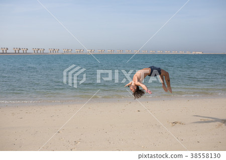 Young man doing somersault on the beach. Young man doing somersault on the beach. 38558130