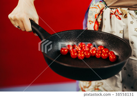 The girl holds a frying pan on which tomatoes lie 38558131