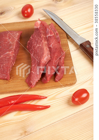 Sliced raw beef on cutting board and vegetables Sliced raw beef on cutting board and vegetables 38558330