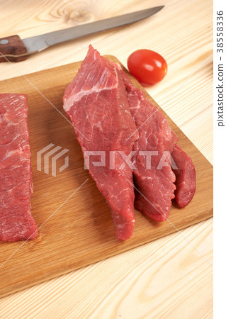 Sliced raw beef on cutting board and vegetables Sliced raw beef on cutting board and vegetables 38558336