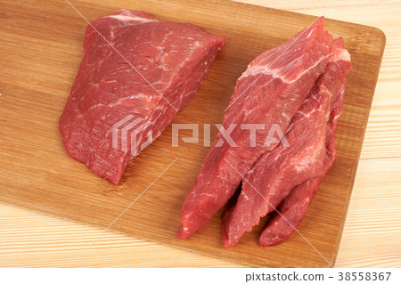 Raw beef piece and slices on wooden cutting board Raw beef piece and slices on wooden cutting board 38558367