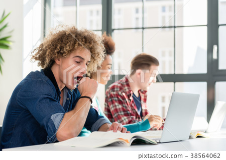 Funny student yawning in front of a book while 38564062