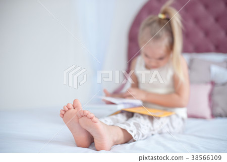 Little blonde girl sitting on the bed reading a Little blonde girl sitting on the bed reading a 38566109