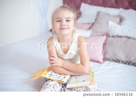 Little blonde girl sitting on the bed reading a Little blonde girl sitting on the bed reading a 38566116