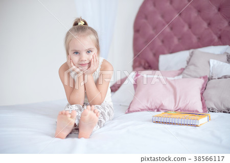 Cute little blond girl sitting on bed Cute little blond girl sitting on bed 38566117