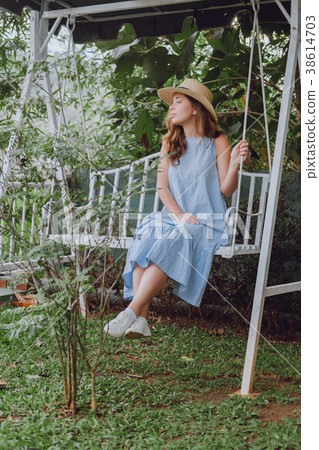 Young woman in a hat sits on a white swing 38614703