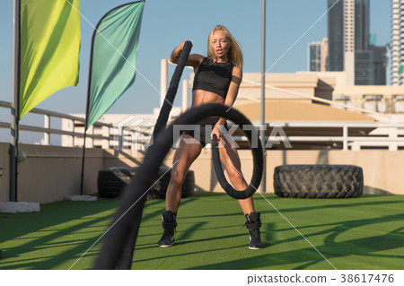 Sports woman doing battle ropes exercises in a 38617476