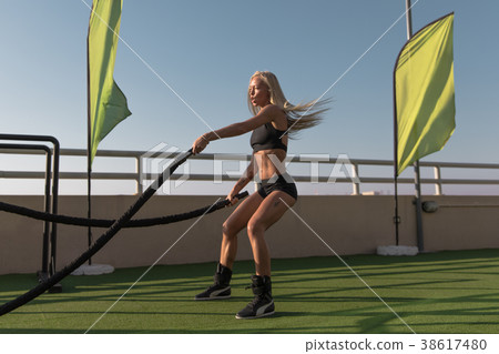 Sports woman doing battle ropes exercises in a 38617480