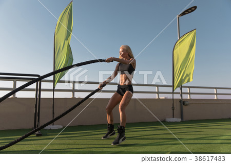 Sports woman doing battle ropes exercises in a 38617483