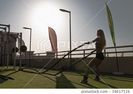 Sports woman doing battle ropes exercises in a 38617516
