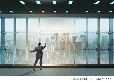 Businessman in front of office window thinking of Businessman in front of office window thinking of 38639367