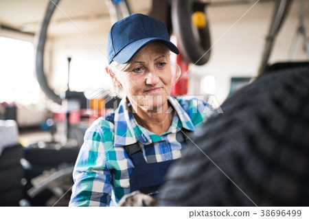 Senior female mechanic repairing a car in a garage Senior female mechanic repairing a car in a garage 38696499