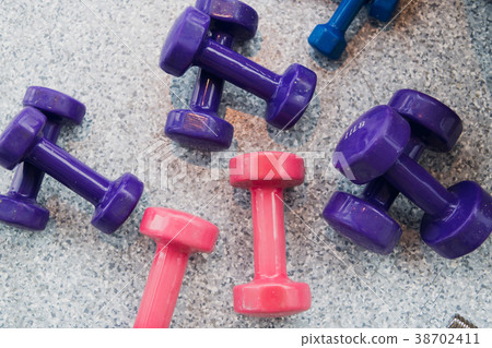 Purple and pink dumbbells lie on the gray floor at Purple and pink dumbbells lie on the gray floor at 38702411