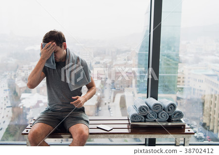 Young man in gym after workout, sitting on a bench Young man in gym after workout, sitting on a bench 38702412