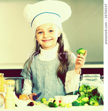Smiling female child in chef cap with vegetables in kitchen Smiling female child in chef cap with vegetables in kitchen 38709147