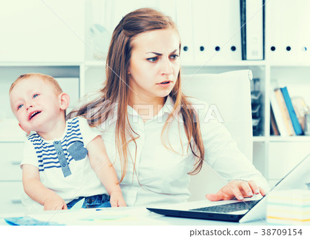 Girl is working with a naughty child in her arms behind a laptop Girl is working with a naughty child in her arms behind a laptop 38709154