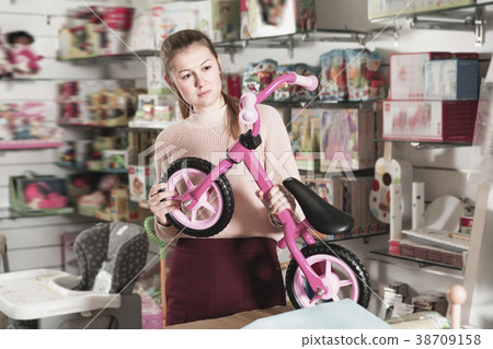 Young woman holding balance bicycle in the shop of goods for chi Young woman holding balance bicycle in the shop of goods for chi 38709158